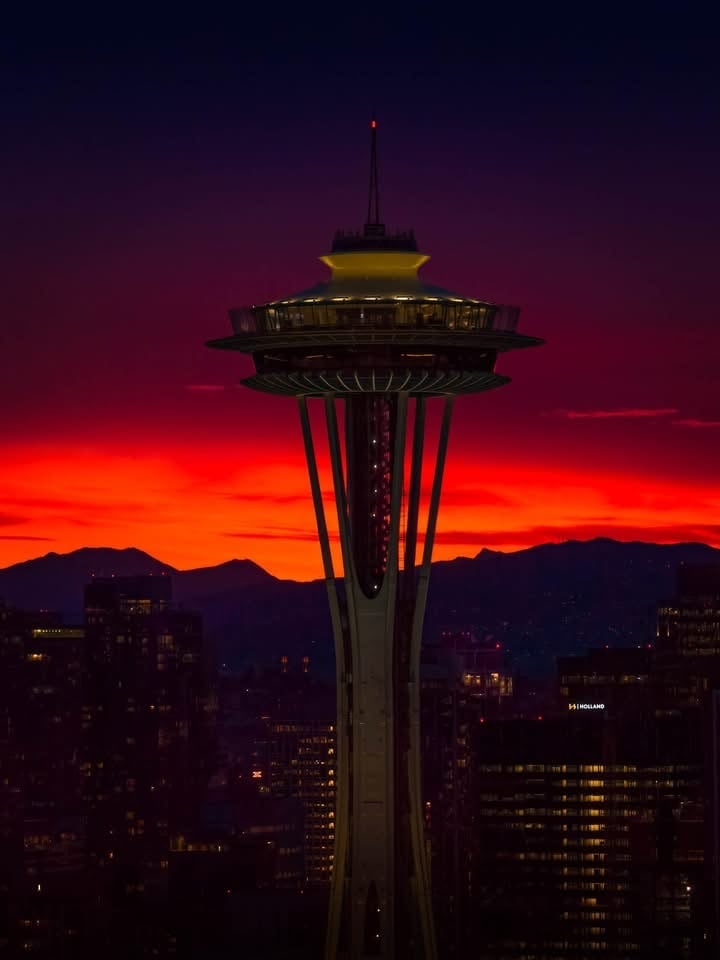 Space Needle tower illuminated at sunset with vibrant red and orange sky above Seattle skyline and mountains