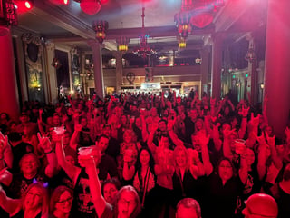 Crowded nightclub dance floor illuminated by red lighting with a large chandelier and ornate venue architecture