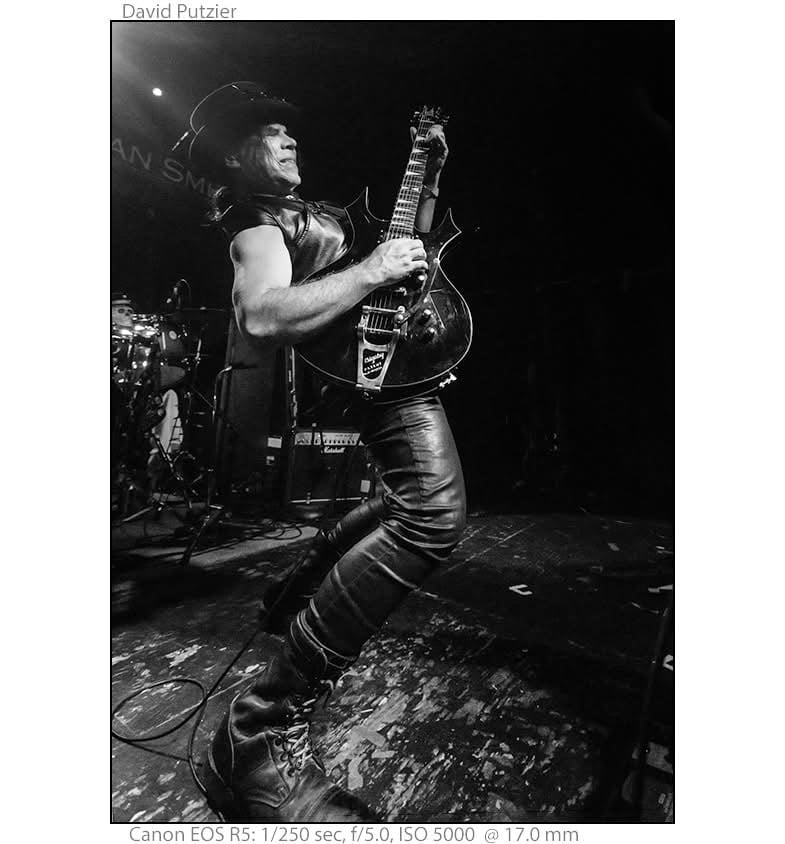 Black and white photograph of a rock musician performing on stage, playing an electric guitar with energetic movement