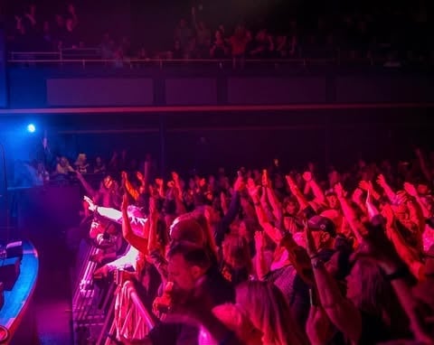 Concert crowd illuminated by red and blue stage lights with performer on left side