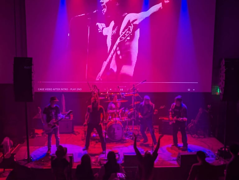 Live band performing on stage with vibrant pink and blue neon lighting, audience members visible in foreground watching the performance